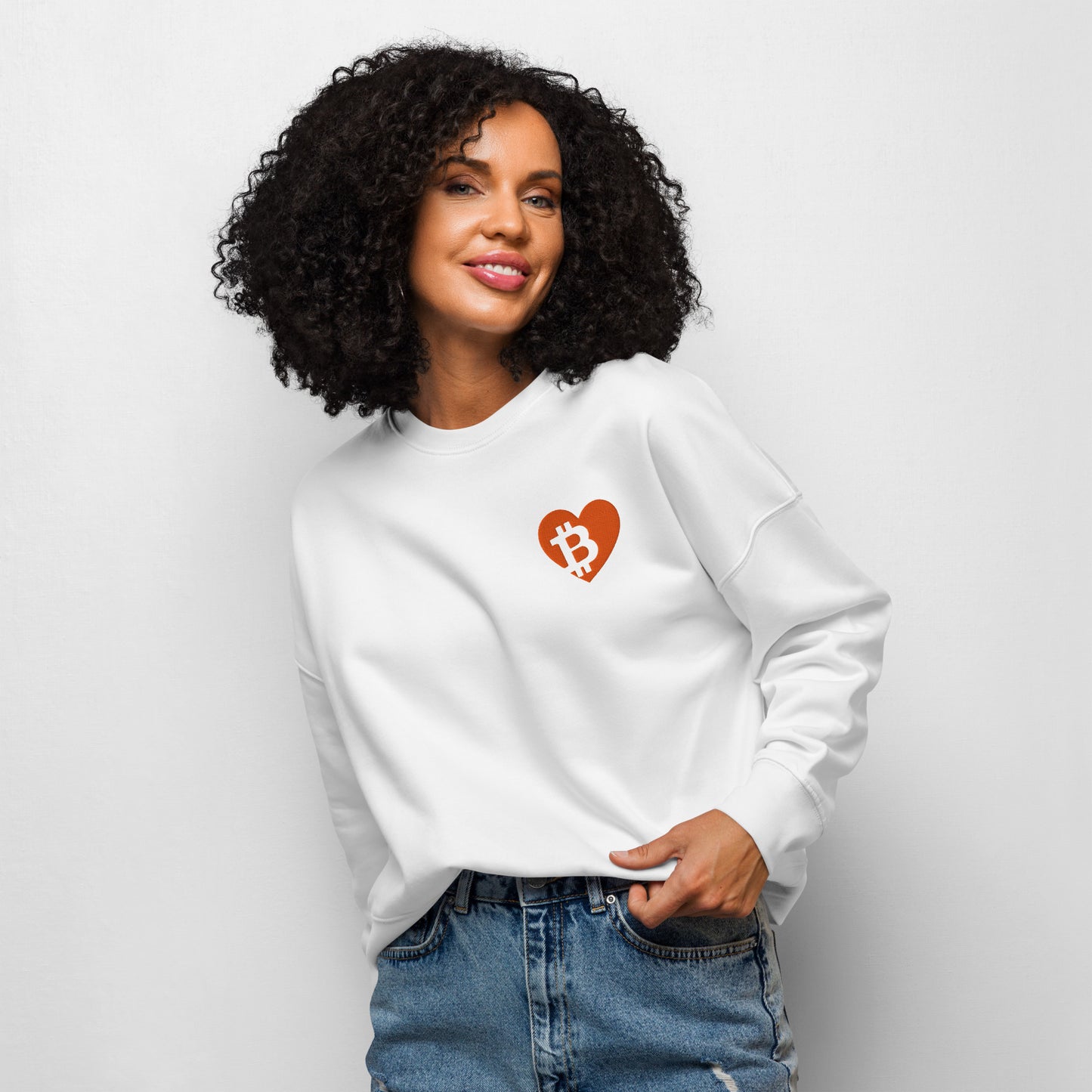 Woman wearing a white sweatshirt with a heart-shaped Bitcoin logo on a plain background