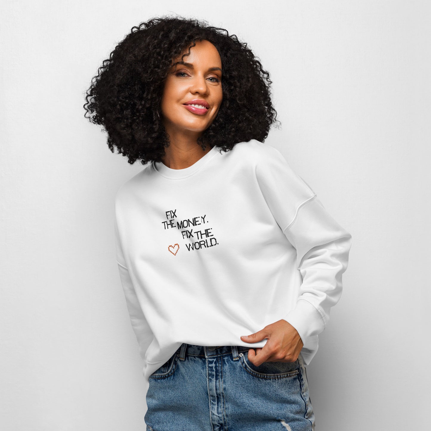 Woman wearing a white sweatshirt with fix the money. fix the world. text and a heart symbol on a plain background