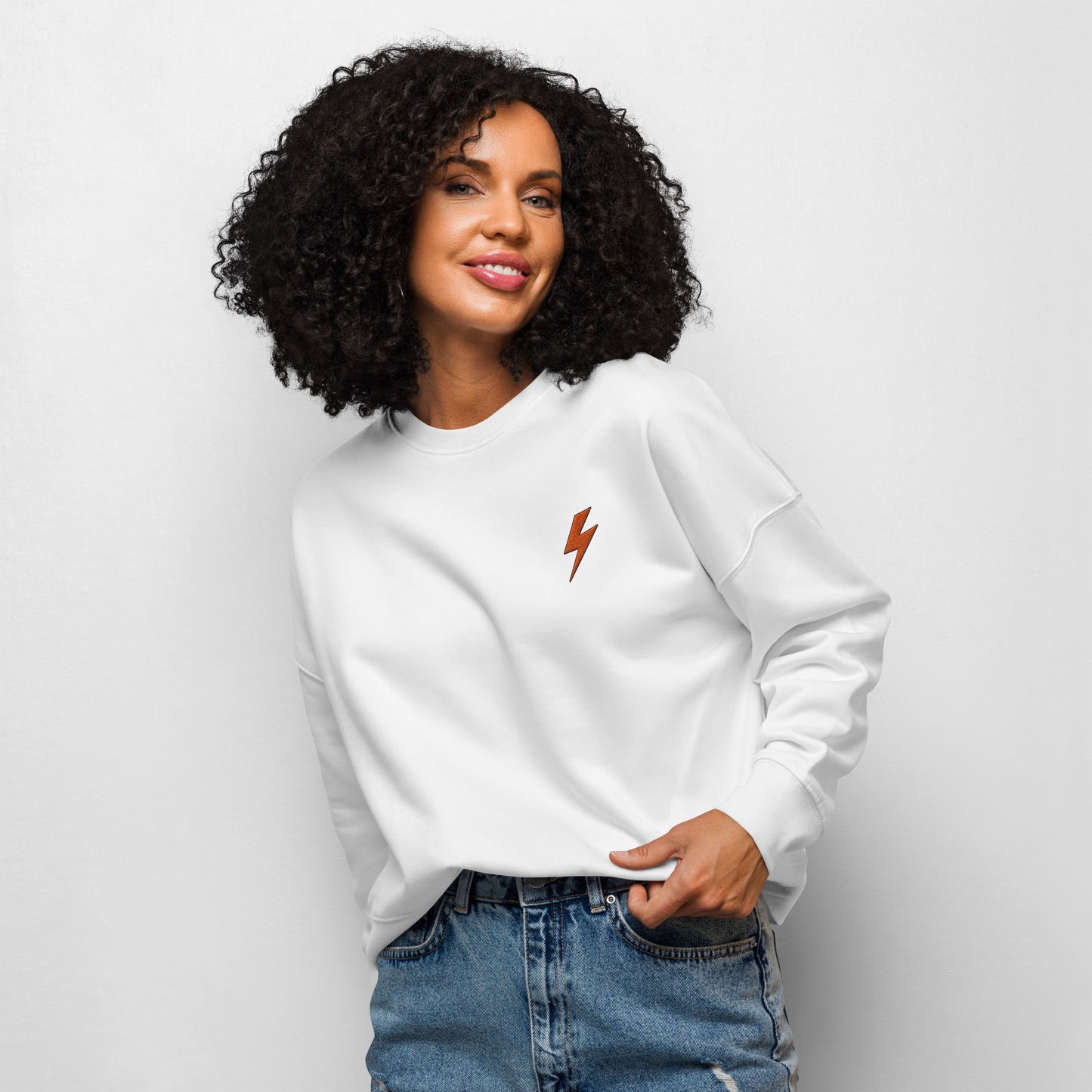 Woman wearing a white sweatshirt with a orange lightning bolt design on a plain background