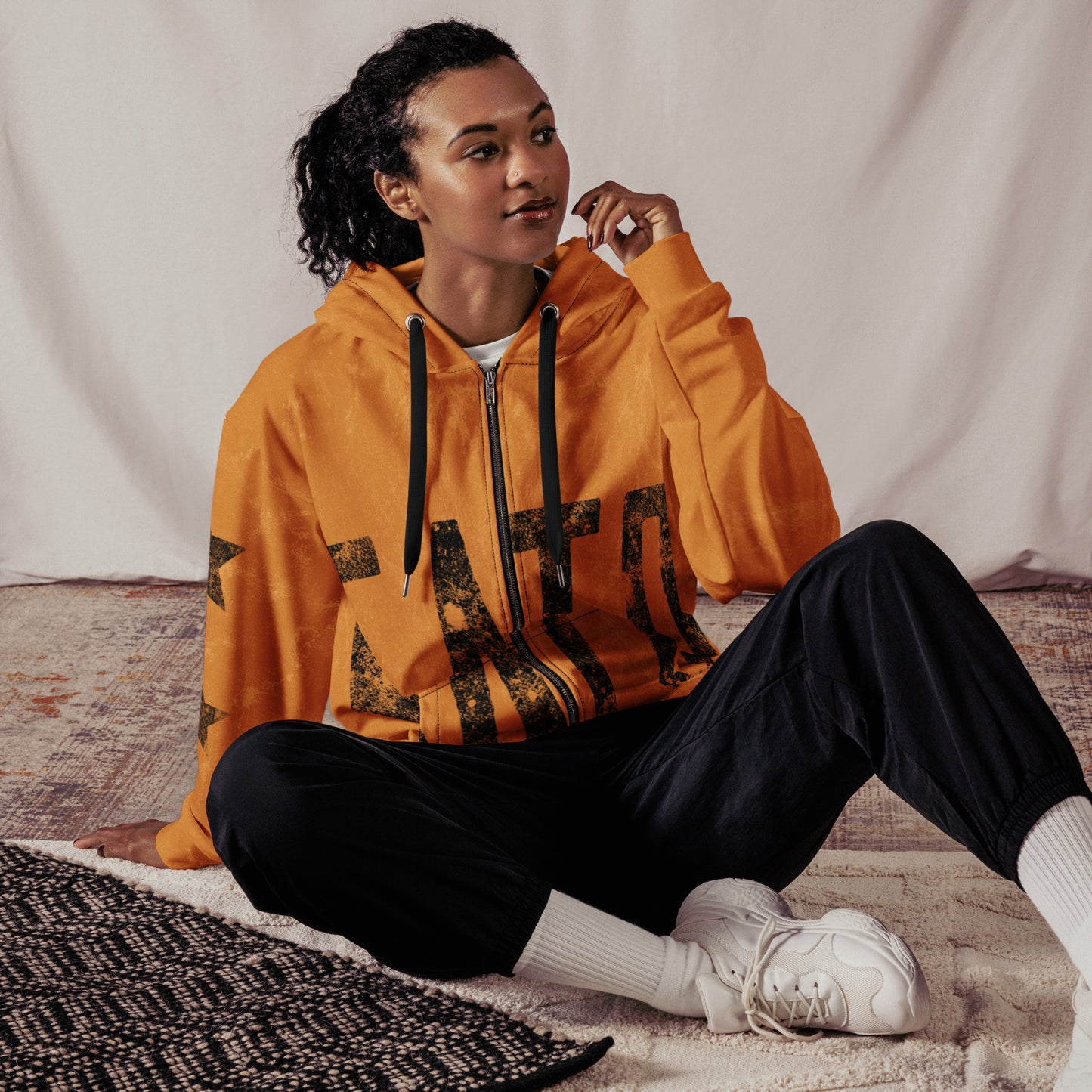 Person wearing an orange hoodie with black satoshi nakamoto text, sitting on a textured surface.