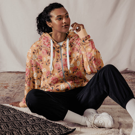 Woman wearing a floral bitcoin pattern hoodie sitting on a textured surface with a neutral background