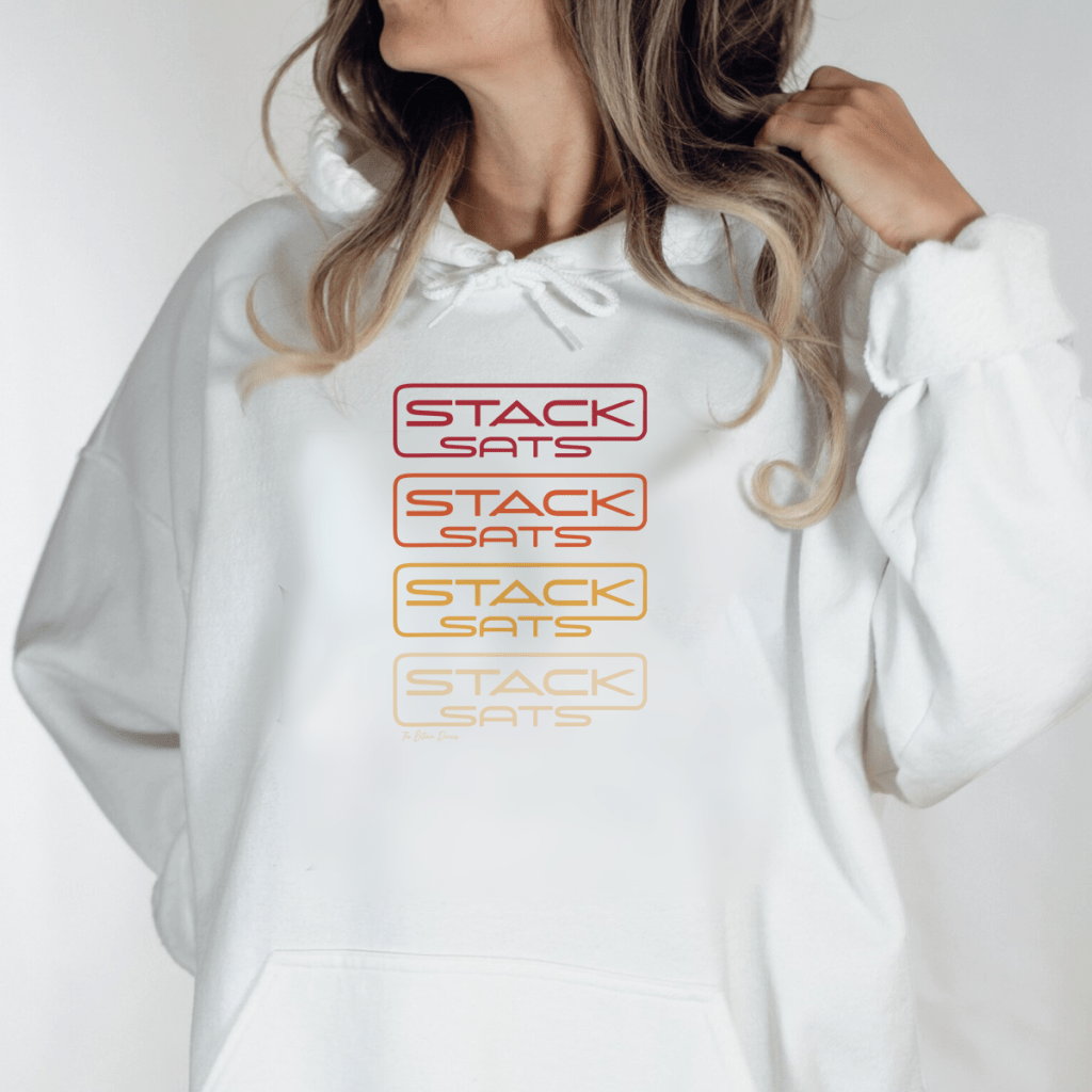 A female model wearing a white hoodie with the words 'stacked sats' repeated on the front in orange hues